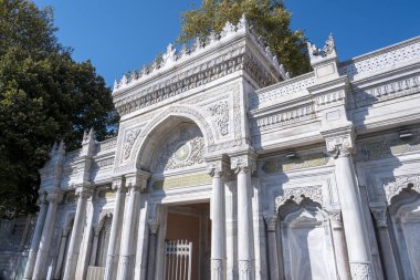 Pertevniyal Valide Sultan Camii 'nin dışı, ağaçlı geniş açılı giriş kapısı, detaylı Osmanlı mimari eserleri, mavi gökyüzü.