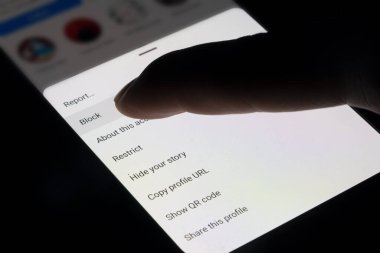 Instagram 'da parmak engelleme düğmesine basın, sosyal medyada birini engelleyin, kötü muamele veya dolandırıcılık fikri, siyah arkaplanlı akıllı telefon ekranı