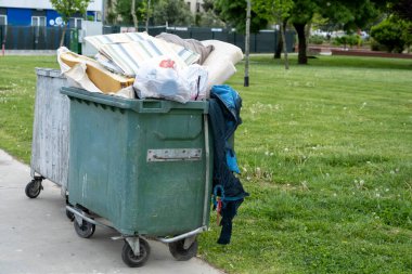 Çöp dolu çöp konteyneri, çevre kirliliği, parktaki yeşil çöp kutusu, kötü geri dönüşüm örneği, açık hava.