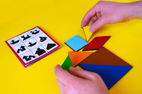 人手玩七巧板和做房子 小孩游戏的概念 黄色背景下孤立的五彩斑斓的形状 玩拼图玩具七巧板 边看边学 — 图库照片
