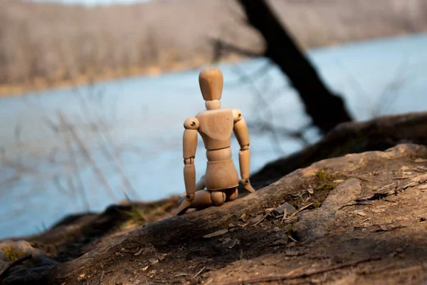 stock image Wooden mannequin sits on tree roots looking to leak, wood puppet daydream, from back, selective focus, autumn concept forest background