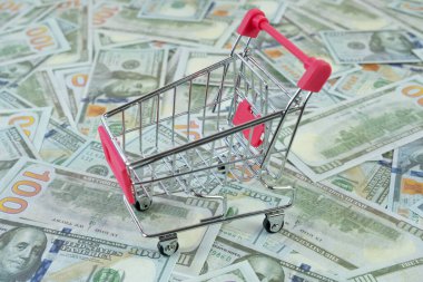 Amerikan dolarları üzerinde süpermarket el arabası, pembe metal market arabası ticareti, minyatür nesneyi, çevrimiçi satış konseptini, market alışveriş fikrini, ABD ekonomisini temsil ediyor.
