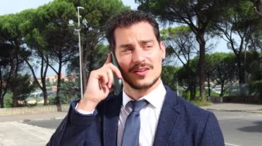 Yakışıklı iş adamı akıllı telefonuyla bir iş görüşmesi yapıyor. Genç işadamı akıllı telefonuyla onun hakkında konuşurken yürüyor..