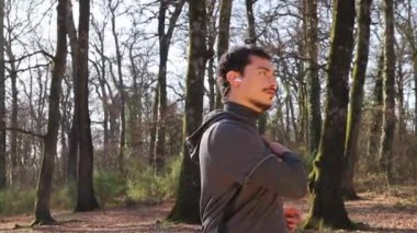 Koşucu müzik dinlerken esniyor. Genç adam ormanda antrenman yapıyor. Spor ve refah kavramı.