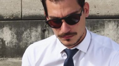 Genç iş adamı dışarıda çalışıyor. Adam merdivenlerde oturuyor ve telefonda konuşuyor..