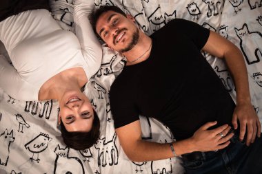 Güzel bir çift yatakta uzanıyor ve kameraya bakıyor. Yukarıdan çekilen genç çift.