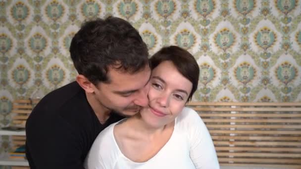 年轻人拥抱着他的女朋友 这对年轻夫妇正坐在床上接吻 — 图库视频影像