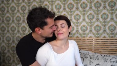 Genç adam kız arkadaşına sarılıyor. Genç çift yatakta oturuyor ve öpüşüyor..