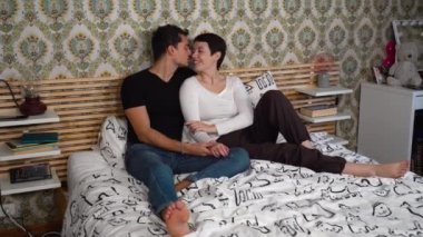 Güzel genç çift yatakta oturuyor ve öpüşüyorlar. Çift sevgisi ve uyum kavramı.