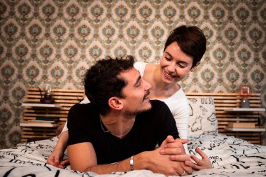 Young couple is lying on the bed and looking at each other happily. Couple and love concept.
