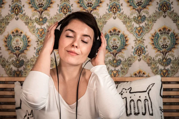 Beautiful woman listens to music in headphones on the bed. The woman has her eyes closed and she is dreaming as she listens to her favorite song about her.