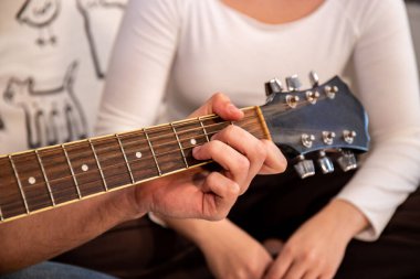 Young man is playing guitar while his girlfriend is singing. Detail of hand on guitar strings.