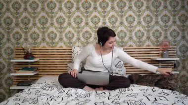 The beautiful woman is relaxing on the bed with her cat. The woman is lying down and she plays with the gray cat while she listens to music.