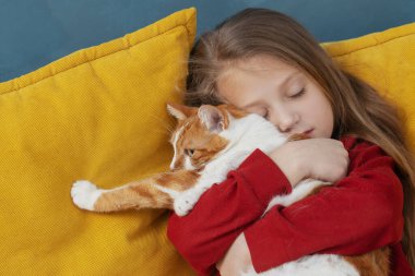 A small cute child gently embraces a red fluffy cat