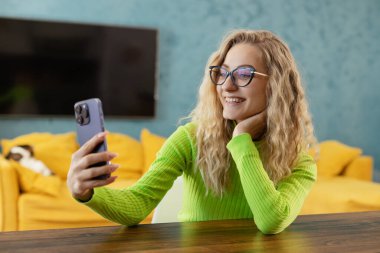 Photo of smiling happy woman wearing eyeglasses using cellphone in room.  Taking a selfie with a cell phone camera. 