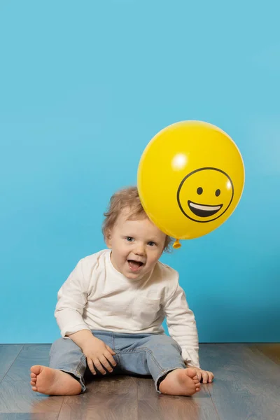 明るい絵文字の笑顔で黄色の風船を保持青い背景にかわいい子供 — ストック写真