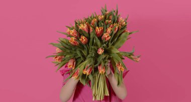 Yüzünün önünde pembe bir demet güzel lale tutan sevimli bir çocuk. Küçük kız annesine buket verdi.