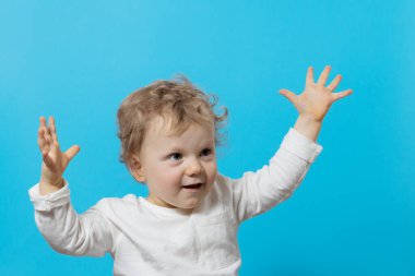 Mavi arka planda, şaşırmış küçük bir erkek bebeğin portresi. Elleriyle yüzünü kapatıyor, saklambaç oynuyor. Çocuk ürünlerinin reklamını yapmak