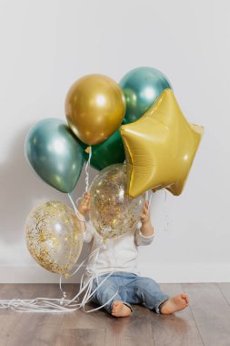 Cute toddler boy in casual clothes with balloons in the room. Advertisement for children's parties.