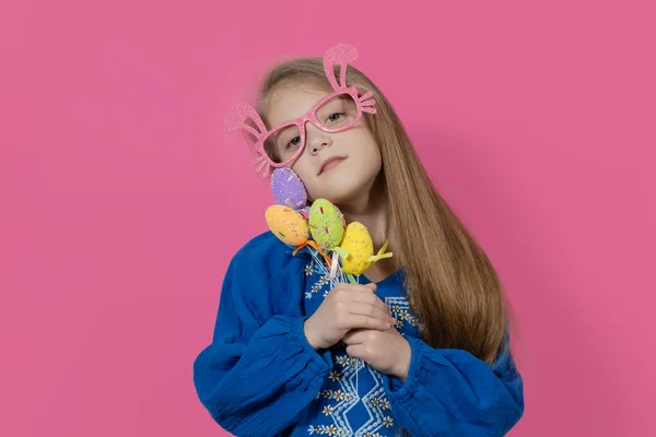 Happy easter! Portrait of funny happy laughing child girl with easter eggs and with bunny-shaped glasses on pink background. funny wow face