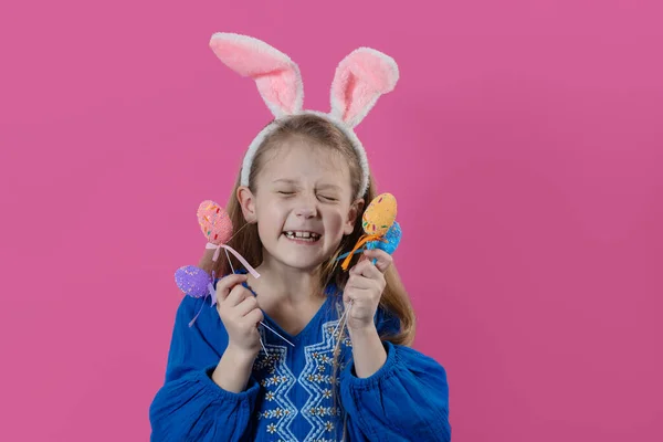 Happy easter! Portrait of funny happy laughing child girl with easter eggs and bunny ears on pink background. funny wow face