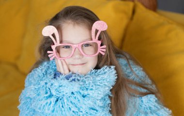 Cute little child girl  in blue fluffy coat wearing bunny ears glasses a on Easter day. Easter girl portrait, funny emotions, surprise.	