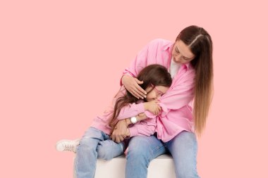 Genç bir anne, küçük tatlı kızıyla oynarken eğleniyor. Kollarını tutuyor, pembe bir arka planda nazikçe sarılıyor.