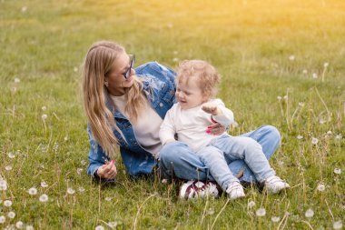 Genç anne parkta küçük oğluyla oynuyor. Karahindibalar çiçek toplar ve üfler