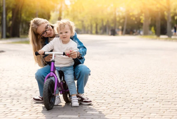 年轻的母亲教她的小儿子如何在公园里骑自行车 — 图库照片