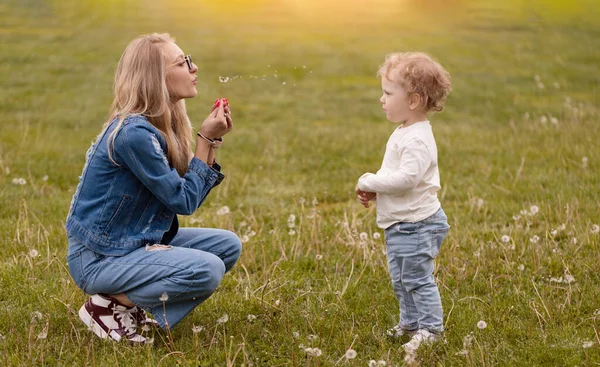 年轻的母亲和她的小儿子在公园里玩耍 蒲公英采花吹风 — 图库照片