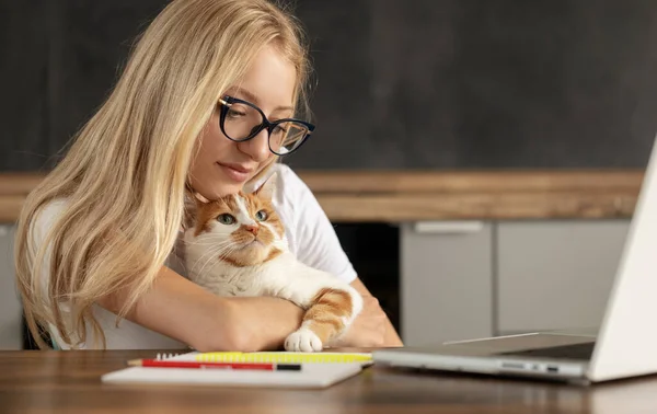 stock image Young woman using laptop and cute cat sitting on the keyboard. Casual girl working on a laptop with her pet while sitting in a homely cozy office.