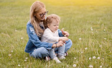 Genç anne parkta küçük oğluyla oynuyor. Karahindibalar çiçek toplar ve üfler
