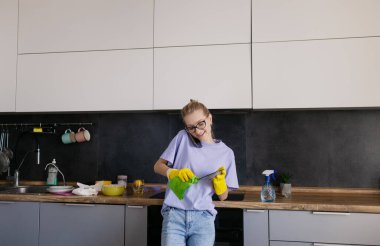 Portrait of  young tired tortured cleaning service woman. Housewife cleaner in yellow rubber gloves stands in the kitchen after a general cleaning of the house