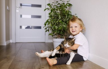 Küçük bir çocuk tüylü hayvanına sarılıyor. Mutlu gülen çocuk evcil kedisine bakıyor, onunla besleniyor ve oynuyor.