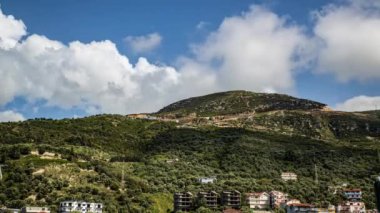 Güneşli bir yaz günüyle güzel bir manzara ve Arnavutluk 'un Vlore kentindeki bir iskan evinin 9. katındaki balkondan gelen Simpsonların bulutlarıyla dolu mavi bir gökyüzü.