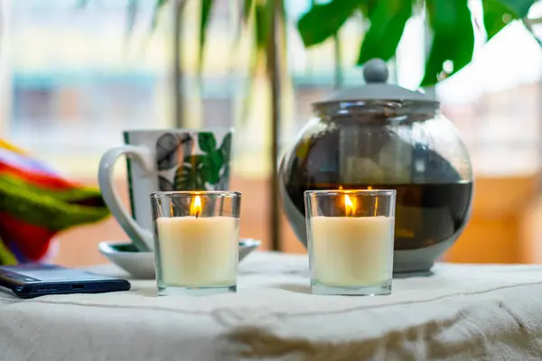 Cozy moment of the day with a cup of hot tea, aromatic candles in the background of a large window, copy space