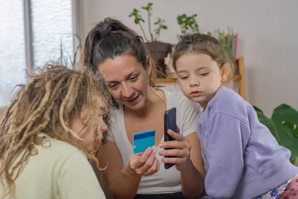 Yetişkin anne ve rastalı çocukları dikkatle dinleyin. Bir banka kartı ve akıllı telefon, eğitim ve finansal teknoloji kopyalama alanı var.