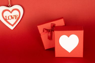 Gift box with hearts on the front where to put pictures or messages including prices, heart detail with the word love with space to add text or other images on an endless red background useful in advertisement. Mockup for valentine's day.