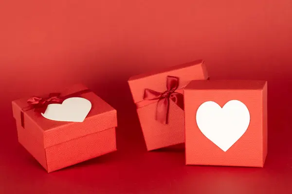 Two gift boxes with hearts on the front where to put pictures or messages including prices, with space to add text or other images on an endless red background useful in advertisement. Mockup for valentine\'s day.