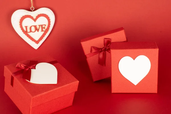Two gift boxes with hearts on the front where to put pictures or messages including prices, heart detail with the word love with space to add text or other images on an endless red background useful in advertisement. Mockup for valentine\'s day.