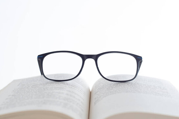 Фотография, посвященная Дню книги: открытая книга на белом фоне со стратегически расположенными черными очками. Визуальная дань силе чтения и литературного видения.
