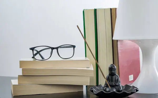 Masanın üzerinde kitap yığını, okuma gözlüğü ve tütsü okuma anı için hazır.