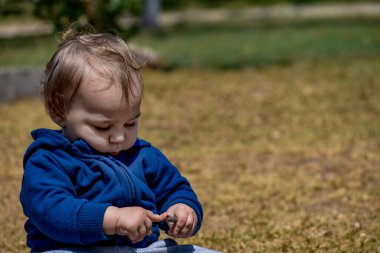 Dışarıdaki hayatı keşfeden, 9 aylık sarışın bir bebek çimlerin üzerinde oturur, etrafındaki doğal harikaları izleyip, merakını keşifler dünyasına yayar..