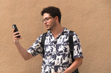 Modern genç adam kentin selfie 'sini yapıyor. Kıvırcık saç, gözlük, baskılı gömlek, şehir modası.