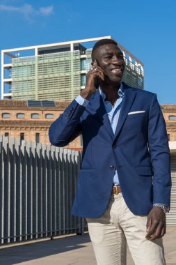 Stil sahibi Afro-Amerikan yönetici, iş alanında şirket binaları ve ofisleri arasında akıllı telefondan konuşuyor..