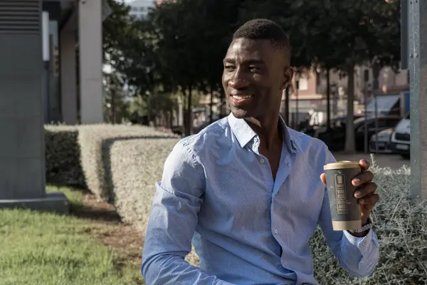 Genç Afro-Amerikalı işadamı, molada kahvenin keyfini çıkarırken gülümsüyor. İş, rahatlama, yaşam tarzı, Afro-Amerikan konuları için ideal.