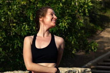 Şehir parkındaki ahşap bir bankta esneme egzersizi yapan genç bir kadın.