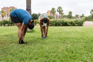 Genç latin adam parkta ayaklarıyla esneme egzersizleri yapıyor.