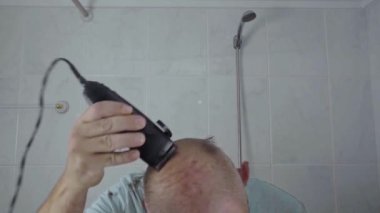 Bir adam saçını traş etmek için elektrikli tıraş makinesi kullanır. Ev bakımının pratik bir sahnesi..