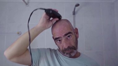 Bir adamın kafasını, aynanın önünde elektrikli makasla tıraş ettiği kişisel bir bakım anı..